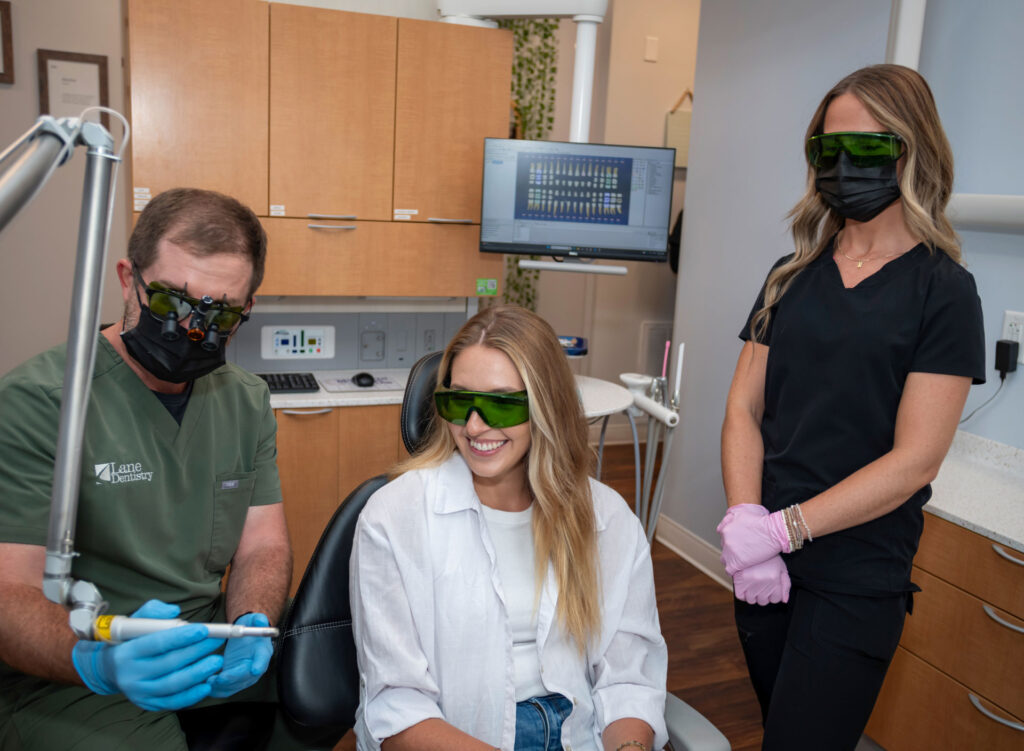 Dr. Lane demonstrating dental tool to patient as assistant looks on