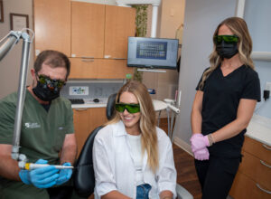 Dr. Lane demonstrating dental tool to patient as assistant looks on